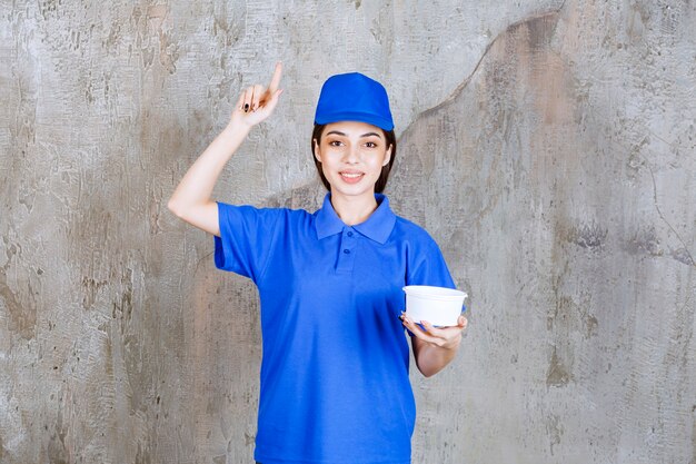 Agente de serviço feminino em uniforme azul segurando uma tigela de plástico e parece confusa e pensativa ou tendo uma boa ideia.
