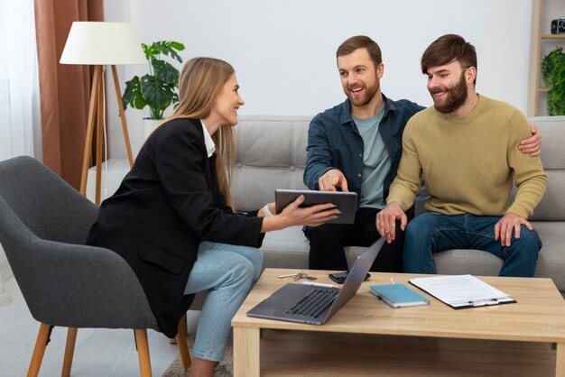 Agente imobiliário feminino falando de negócios e mostrando a casa para o casal gay