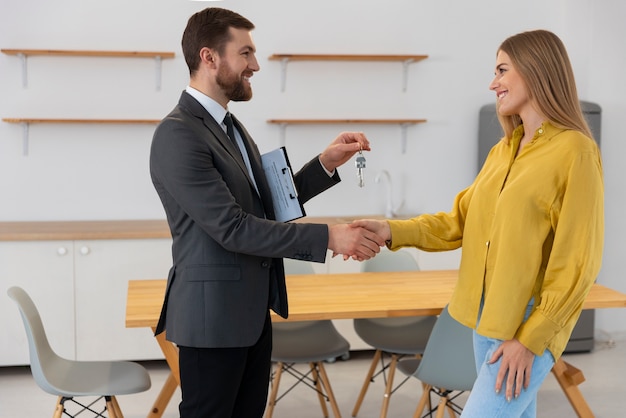 Agente imobiliário masculino dando as chaves da nova casa para o comprador feminino