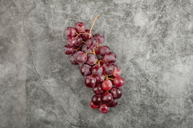 Aglomerado de uvas maduras frescas vermelhas na superfície de mármore.