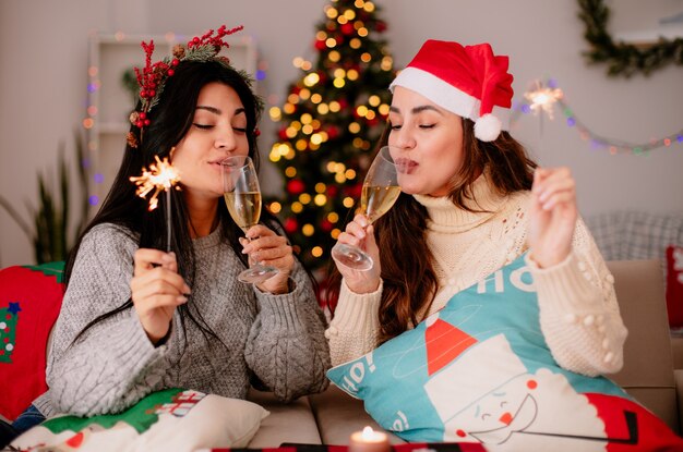 agradar as lindas meninas com chapéu de Papai Noel bebem taças de champanhe e seguram estrelinhas sentadas nas poltronas, aproveitando o Natal em casa