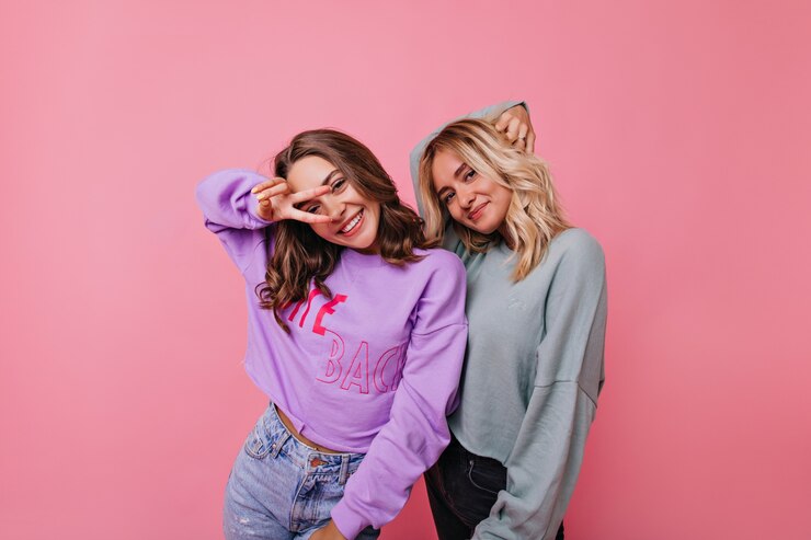 Foto grátis agradáveis jovens senhoras encaracoladas posando na bela rosada. retrato de irmãs alegres usa roupas da moda.