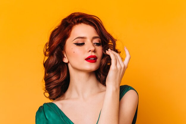 Agradável modelo feminino posando no espaço amarelo. Foto de estúdio da romântica garota ruiva com vestido verde.