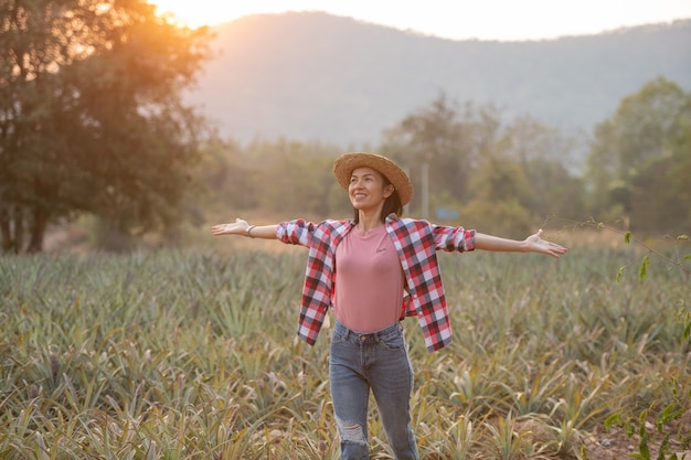Foto grátis agricultor feminino asiático ver crescimento de abacaxi na fazenda, mulher jovem e bonita agricultora em pé em terras agrícolas com os braços levantados felicidade exultante e alegre.