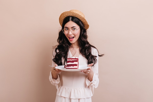 Ainda bem que mulher asiática segurando o prato com bolo. Foto de estúdio de mulher chinesa com chapéu de palha.