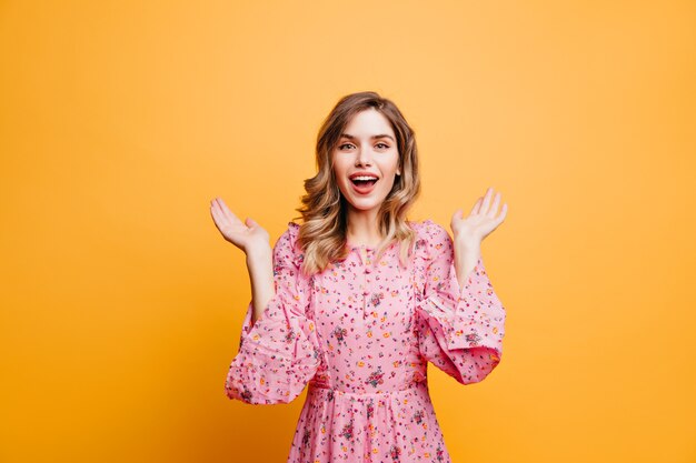 Ainda bem que mulher atraente com penteado romântico arrepiante Garota bonita animada posando na parede amarela.