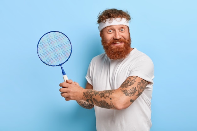Ainda bem que o jogador de esportes segura uma raquete de tênis, usa uma faixa branca na cabeça, camiseta