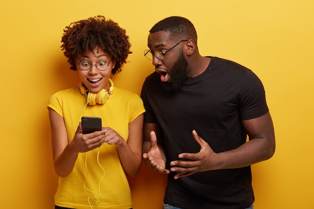 Foto grátis ainda bem que uma mulher afro a olhar para um dispositivo smartphone ligado a auscultadores