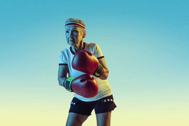 Foto grátis ainda chutando. mulher sênior em roupas esportivas boxe em gradiente