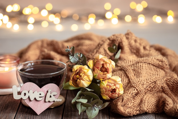 Ainda vida festiva adora com uma bebida em um copo, flores e detalhes de decoração em uma superfície de madeira contra um fundo desfocado com bokeh.