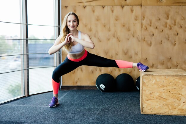 Ajuste a caixa de jovem pulando em um ginásio de estilo crossfit. Atleta feminina está realizando saltos de caixa no ginásio.