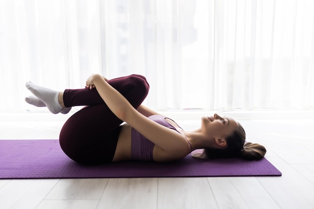 Ajuste a flexibilidade da mulher, esticando a perna e as costas para se aquecer fazendo exercícios de ginástica aeróbica em casa.