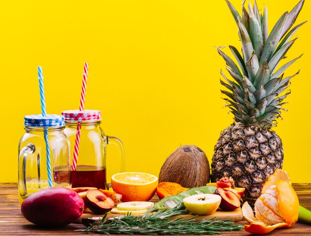Alecrim; coco; frutas e suco na caneca mason jar na mesa de madeira contra um fundo amarelo
