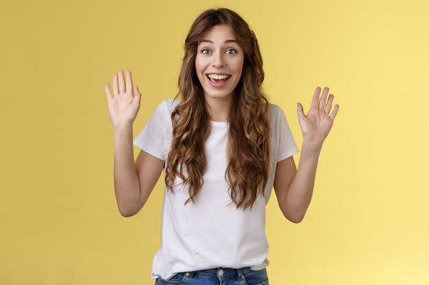 Alegre, alegre, extrovertido, bonito, positivo, jovem, sorrindo, amplamente, levante ambas as palmas das mãos acenando com as mãos Olá gesto de saudação bem-vindo amigo convidado sorrindo oi com prazer convide venha dentro de fundo amarelo