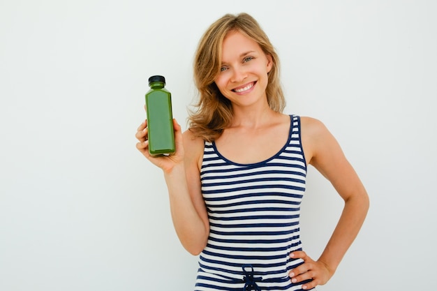 Alegre bela jovem recomendando bom shampoo e olhando a câmera em frente ao fundo branco. retrato de mulher feliz segurando mão no quadril e mostrando novo produto. conceito de escolha