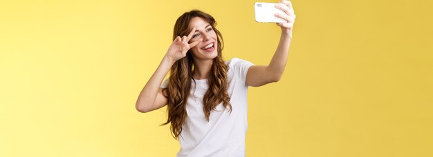 Alegre carismática bonita mulher de cabelos ondulados camiseta branca mostra paz sinal de vitória sorrindo