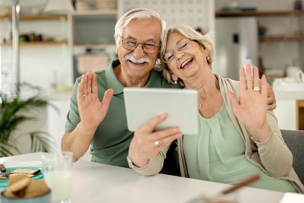 Alegre casal maduro acenando durante a chamada de vídeo no touchpad