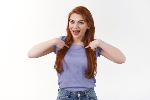 Alegre, divertida, sorridente, ruiva, caucasiana, de camiseta roxa, apontando para o peito e sorrindo, falando de realização pessoal, gabando-se, voluntária, sugerir candidatura, parede branca