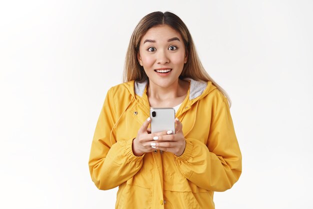 Alegre divertido sorridente feliz jovem asiática loira fascinada olhar encantado câmera boba segure o smartphone não pode parar de jogar legal interessante novo jogo de telefone blogueiro viciado em mídia social