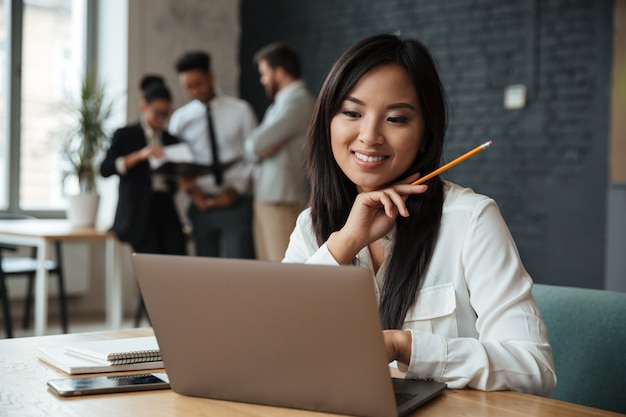 Alegre empresária asiática jovem usando laptop