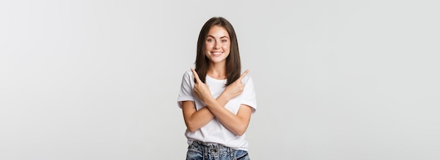 Foto grátis alegre garota atraente apontando os dedos para o lado mostrando duas variantes