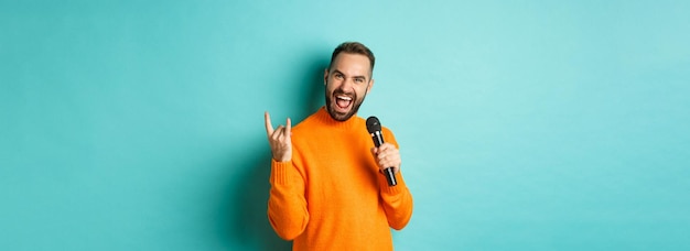 Foto grátis alegre homem bonito cantando música no microfone mostrando gesto rocknroll animado em pé sobre turqu