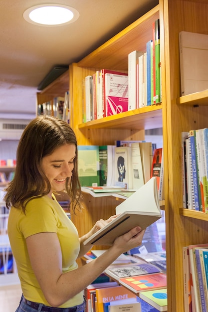 Foto grátis alegre, menina adolescente, leitura, perto, bookcase