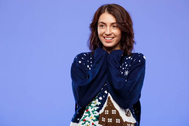 Alegre menina morena linda alegre camisola de malha aconchegante sorrindo posando sobre parede azul