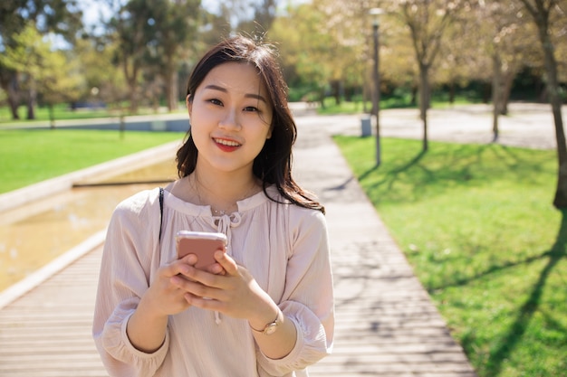 Alegre menina positiva com celular posando ao ar livre