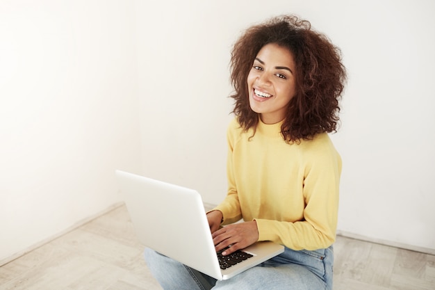 Foto grátis alegre mulher africana bonita sorrindo sentado com o laptop no chão.