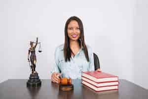 Foto grátis alegre mulher afro-americana na mesa com martelo, livros e estátua