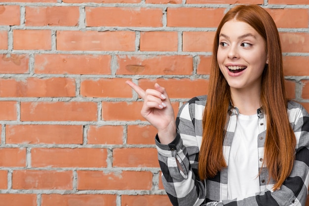 Alegre mulher apontando para parede de tijolo