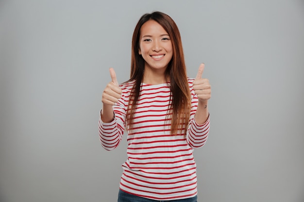 Alegre mulher asiática mostrando os polegares com as duas mãos