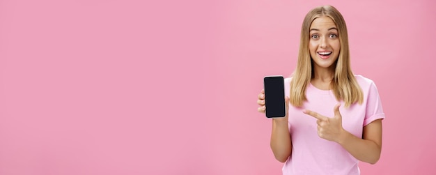 Foto grátis alegre mulher atraente e agradável promovendo aplicativo legal ou smartphone segurando celular e pointi