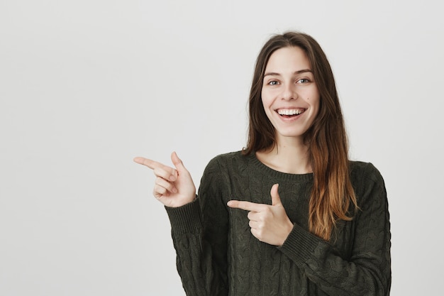 Alegre mulher bonita, apontando os dedos para a esquerda, convidando