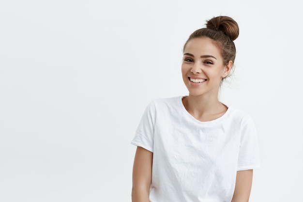 Alegre mulher caucasiana bonita com penteado coque vestindo camiseta, expressando alegria e bom humor