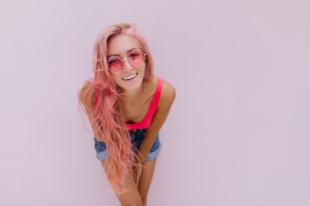 Alegre mulher caucasiana com cabelo rosa, posando com um sorriso fofo.