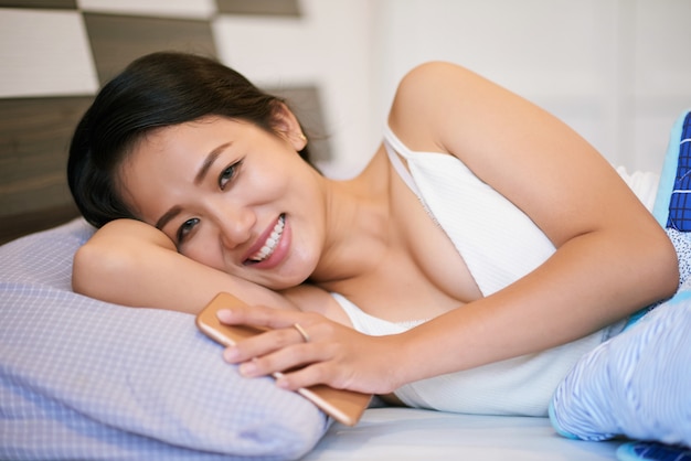 Alegre mulher com telefone, deitada na cama