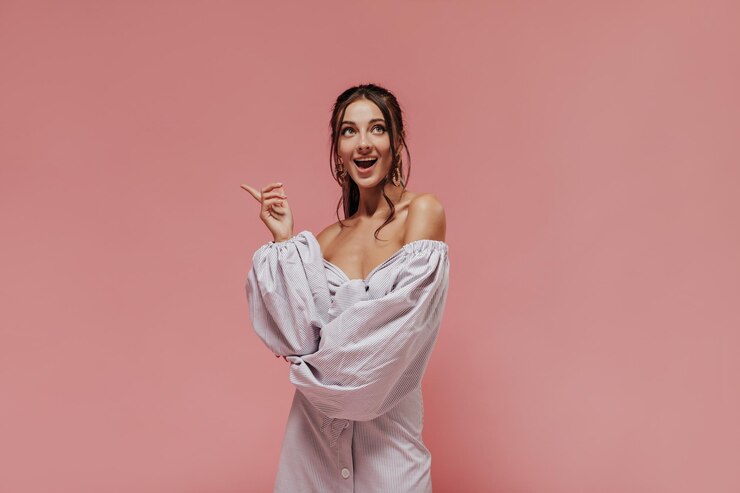 Foto grátis alegre mulher de cabelos negros em acessórios elegantes e roupas leves modernas listradas olhando para cima e posando em pano de fundo isolado