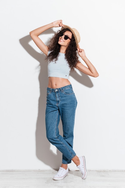 Alegre mulher de jeans chapéu e óculos de sol, sorrindo para a câmera