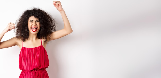 Foto grátis alegre mulher emotiva com cabelo encaracolado vestido vermelho levantando as mãos e cantando torcendo pelo time shou