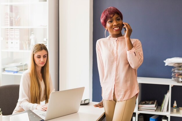 Alegre mulher falando no telefone perto de colega