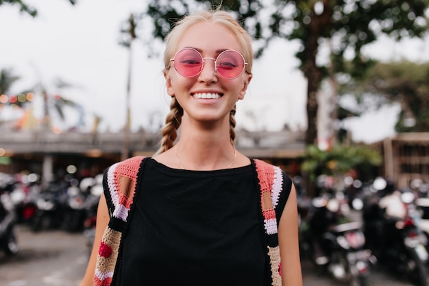 Foto grátis alegre mulher loira em traje de malha, passar o tempo ao ar livre. mulher com tranças loiras, óculos cor de rosa.