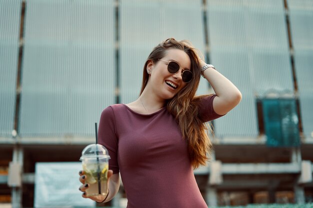 Alegre mulher na rua bebendo bebida refrescante de manhã