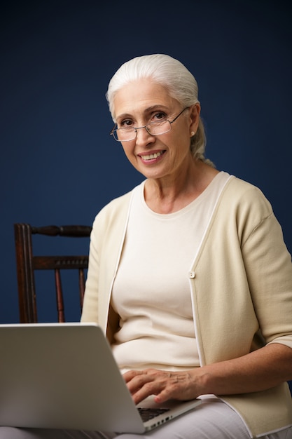 Alegre mulher velha usando computador portátil.