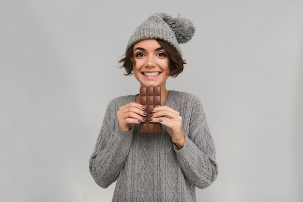 Alegre mulher vestida de camisola e chapéu quente, segurando o chocolate.