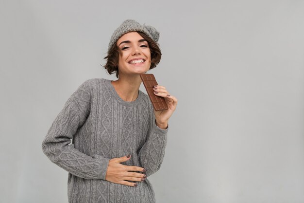 Alegre mulher vestida de camisola e chapéu quente, segurando o chocolate.