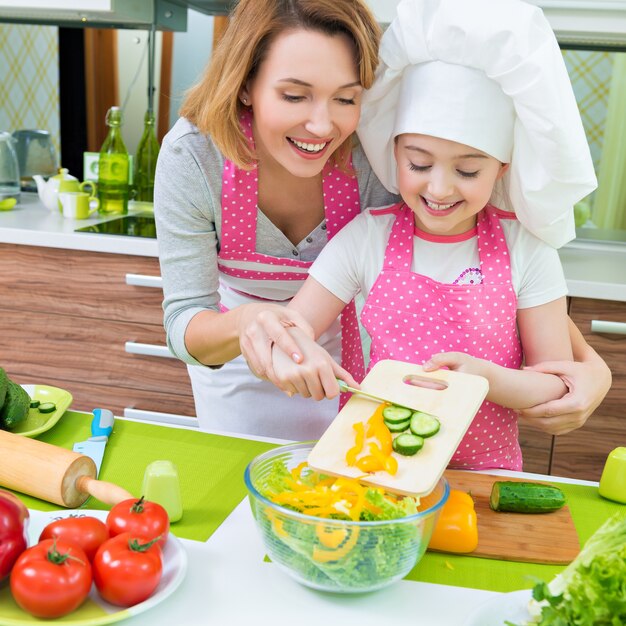 Alegre sorridente mãe e filha cozinhando uma salada na cozinha.