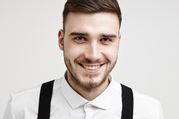 Alegria, emoções positivas e conceito de sentimentos. Cabeça e ombros de um jovem noivo bonito e alegre com barba por fazer e covinhas, sorrindo alegremente para a câmera e se sentindo feliz por se casar hoje