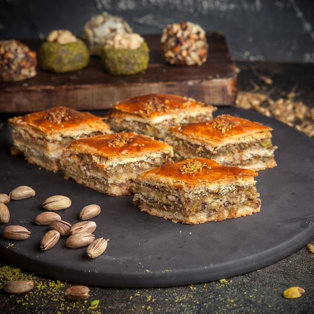 Algum baklava com os biscoitos no fundo em uma vista lateral da plataforma arredondada preto.